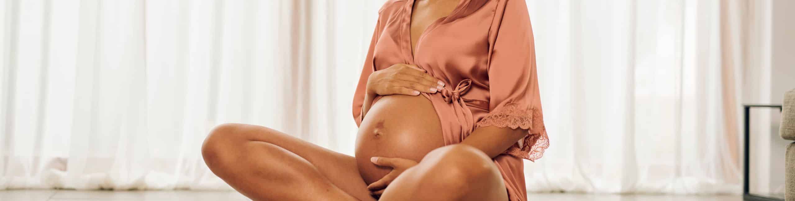 Trudnica sjedi na podu i miluje svoj trbuh.