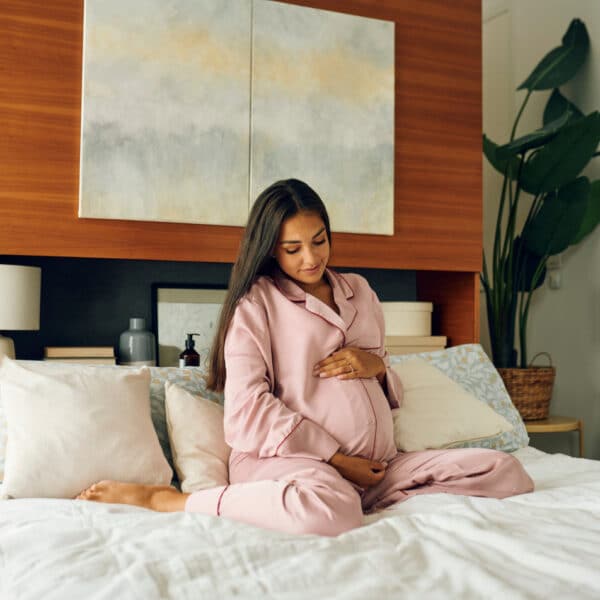 Trudnica sjedi u krevetu i dodiruje svoj trbuh - važnost vitamina u trudnoći