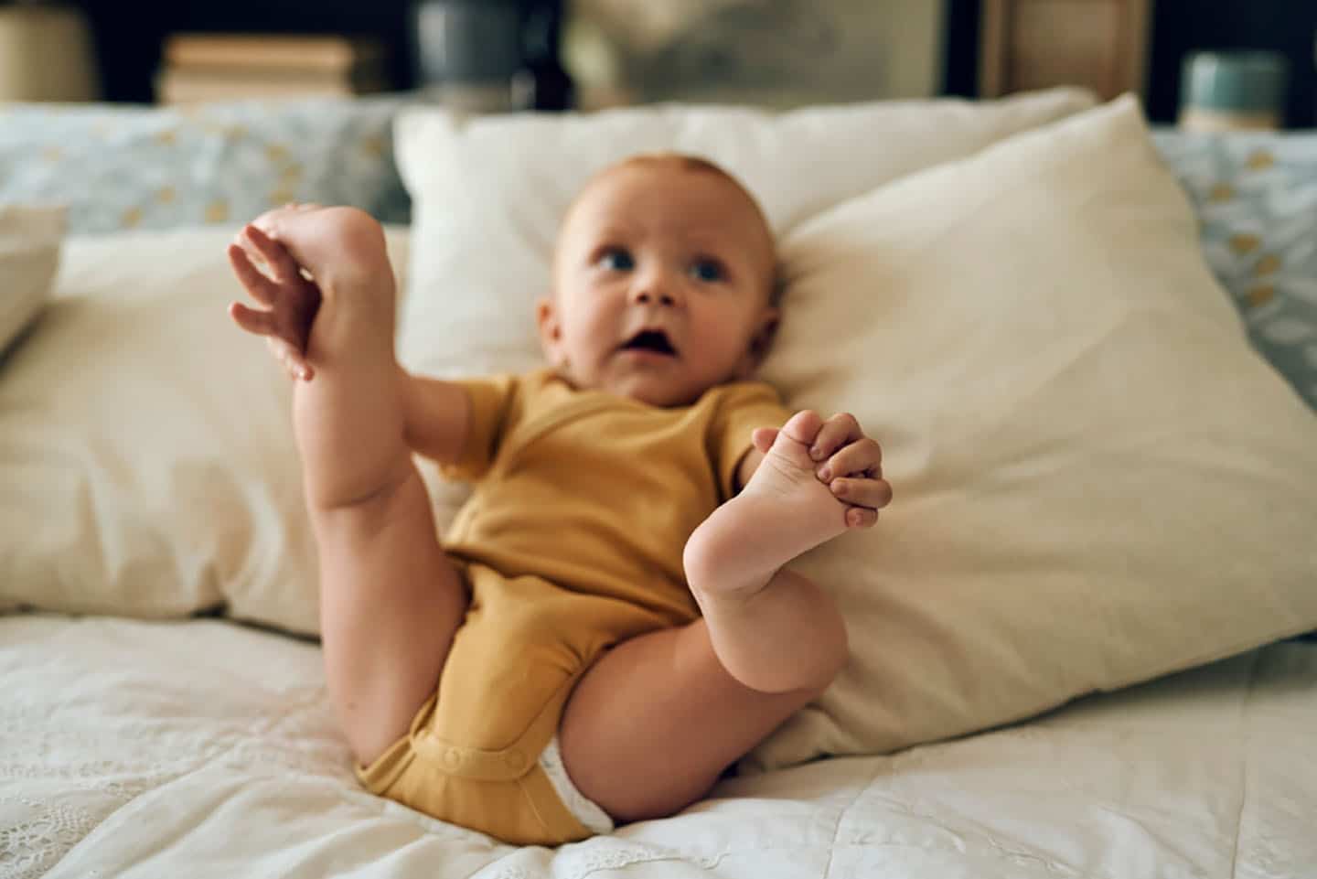 Beba leži na krevetu s podignutim nogama