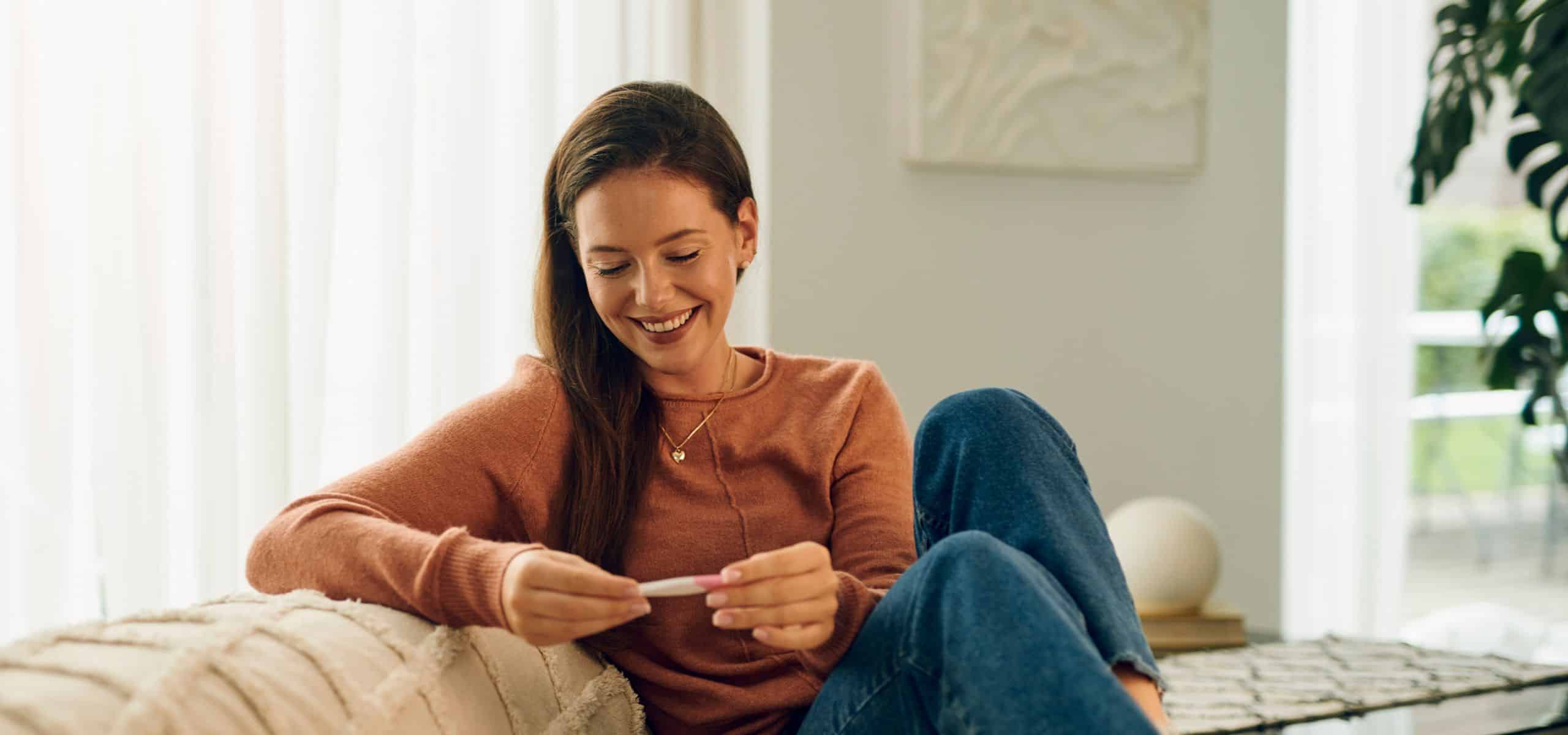 Trudnica sjedi na kauču gledajući pozitivan test na trudnoću dok planira trudnoću