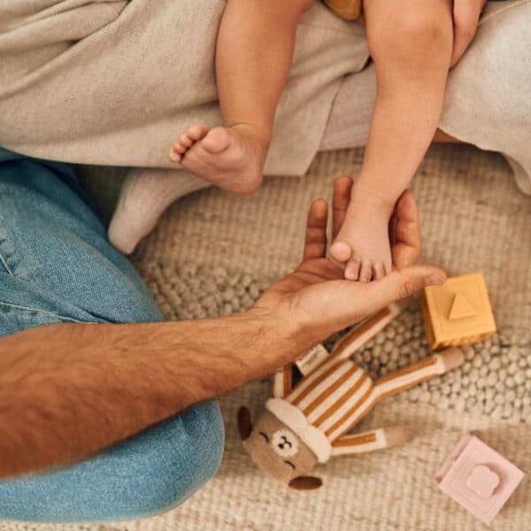 Tata drži bebino stopalo, mekani tepih i igračke